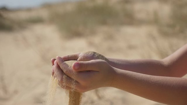 Woman`s hands raising sand in a handfull on a sea coast on a sunny day in slo-mo 