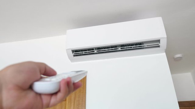 Flat air conditioner on white wall in room. Pushing button on remote. Setting temperature