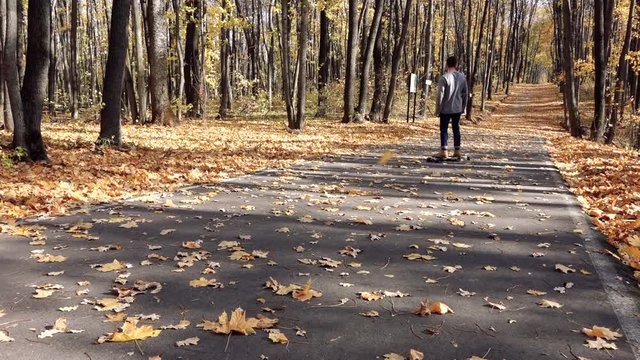 a man descends on a longboard uphill on asphalt covered with leaves