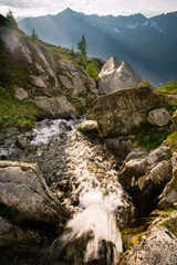 A waterfall in an alpine meadow catching the golden light of sunset in the mountains - 297072954