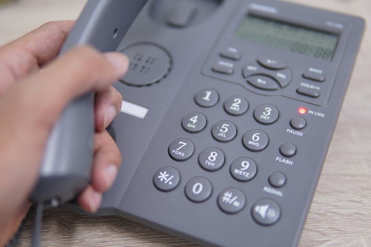 Male Hand Holding Telephone And Dailing A Phone Number.	