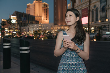 young beautiful local girl standing at night with mobile phone by las vegas skyline. charming lady in dress using cellphone texting on city street while waiting for her friend to club together. © PR Image Factory