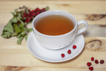 White cup of tea with plate and dry rowan berries horizontal wooden background
