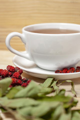 White cup of tea with plate and dry rowan berries wooden background macro