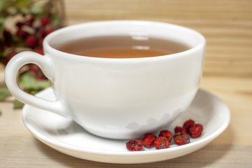 White cup of tea with plate and dry rowan berries wooden background closeup
