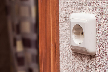 Single electric European outlet on the wall with wallpaper near the door.
