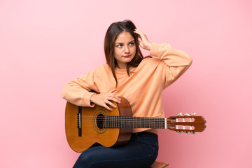 Young brunette girl with guitar over isolated pink background having doubts and with confuse face...