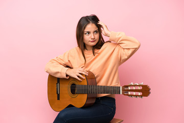 Fototapeta premium Young brunette girl with guitar over isolated pink background having doubts and with confuse face expression
