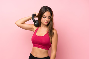 Young sport girl over isolated pink background making weightlifting with kettlebell