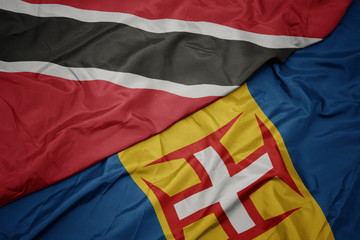 waving colorful flag of madeira and national flag of trinidad and tobago.