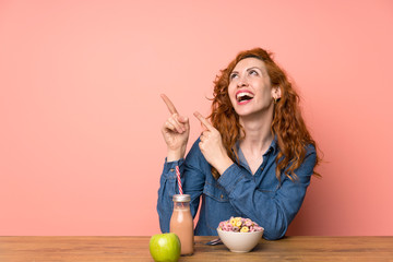 Redhead woman having breakfast cereals and fruit pointing with the index finger a great idea