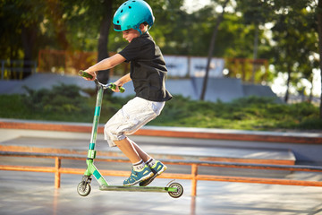 A boy on a scooter and in protective helmet do incredible stunts in skate park. Extreme jump. The...