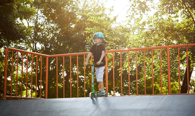 A boy on a scooter and in protective helmet do incredible stunts in skate park. Extreme jump. The...