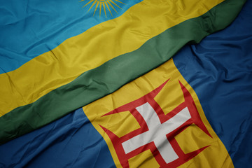 waving colorful flag of madeira and national flag of rwanda.