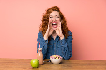 Redhead woman having breakfast cereals and fruit shouting with mouth wide open