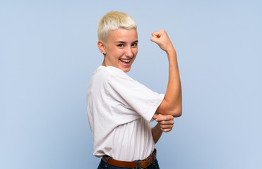Teenager girl with white short hair over blue wall doing strong gesture