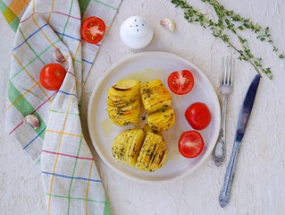 Hasselback potatoes on a white clay plate on a light concrete background. Potato recipes. Thanksgiving Day. Scandinavian cuisine. Top view.