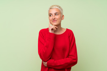 Teenager girl with white short hair over green wall thinking an idea while looking up