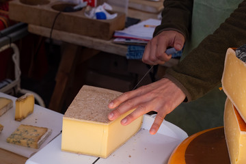 Market stall worker slicing cheese with a wire cutter