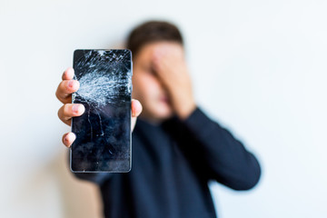 Kid holding broken smartphone covering his face with hand shocked with shame for mistake,...