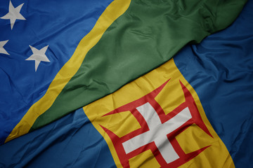 waving colorful flag of madeira and national flag of Solomon Islands .