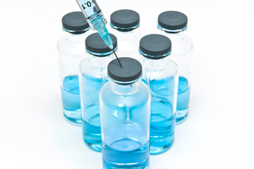 Close up of syringe and medical vials containing blue liquid medicine on the white background