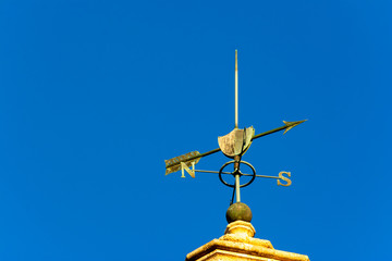 Sunset lit weather vane on clear blue sky