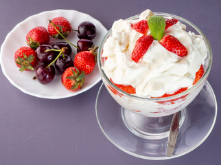 Strawberries with whipped cream in a glass bowl and berries in the background