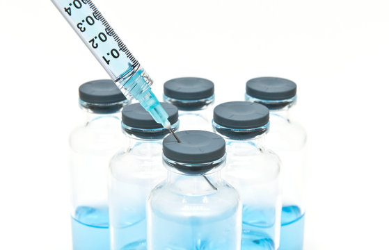 Close up of syringe and medical vials containing blue liquid medicine on the white background