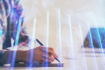 A woman hands writing information about stock market in notepad. Forex chart holograms in front. Concept of research. Double exposure