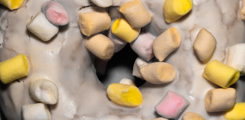 Close up top view on donut or doughnut with white frosting and colorful marshmallow topping.