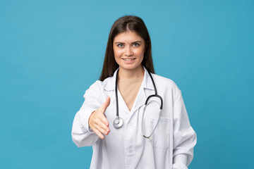 Young woman over isolated blue background with doctor gown and making a deal