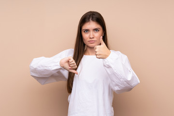 Young girl over isolated background making good-bad sign. Undecided between yes or not