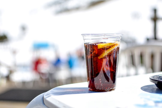 Plastic glass with fizzy cola soda, lemon and ice on white table. Large aperture, blurred background. Ski resort of Pas De La Casa, Andorra -Image
