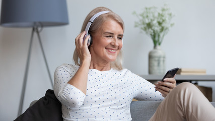 Smiling mature woman wear wireless headphones looking at phone screen