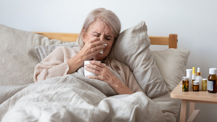 Older ill woman holding handkerchief blowing nose in bed