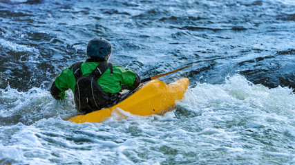 Canoer in a yellow kayak doing white water rafting
