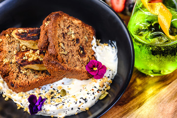 Two slices of Banana Bread on a bed of Tahini Yoghurt with grilled bananas in a bowl and next to a green drink