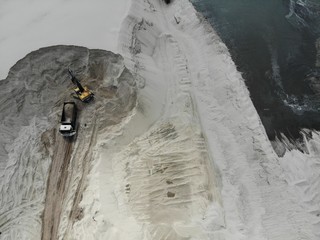 Bulldozer is working on a sand. The view is from the top. Aerial shot from the drone on industrial process of loading the truck with white sand. Getting a natural material from the lake.