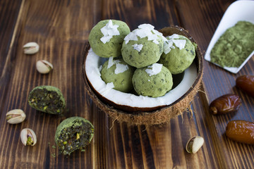 Energy balls with  matcha powder, pistachios, dates  and coconut chips in the half coconut on the brown  wooden background. Closeup.