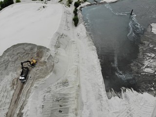 Single bulldozer is working on a sand. The view is from the top. Aerial shot from the drone on industrial process of loading the truck with white sand. Getting a natural material from the lake.