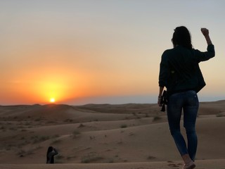 Young Lady is in the middle of the dessert, she had a dune drive and niw is is wstching a beautiful sunset.