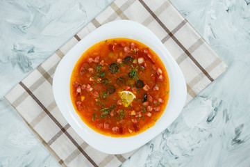 Traditional Russian hodgepodge with ham, olives and lemon in white bowl on gray background. Russian solyanka