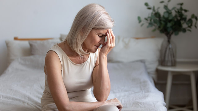 Older woman sit on bed coping with morning headache concept