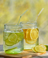 Two glass with lemonade or mojito cocktail with lemon and mint, cold refreshing drink or beverage with ice on rustic blue background. Copy space