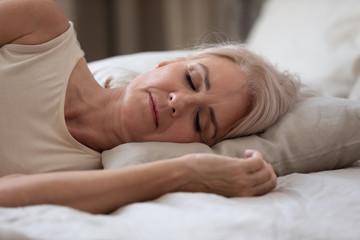 Fototapeta na wymiar Calm serene older woman sleeping alone in bed, closeup view
