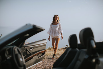 Pretty young woman by the white cabriolet car on the seaside