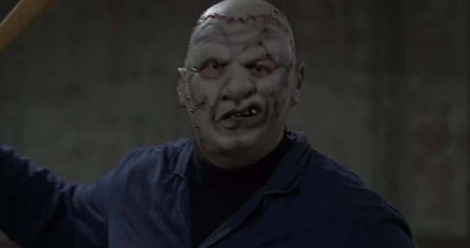 Extremely dangerous man in mask of movie maniac attacks spectator with baseball bat, psycho in parking lot, Halloween holiday, creepy costume, October walk, red ball in his hand, alien from hell