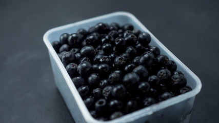 Owoce aronii w przeźroczystym pudełku. Ciemne tło, zbliżenie.