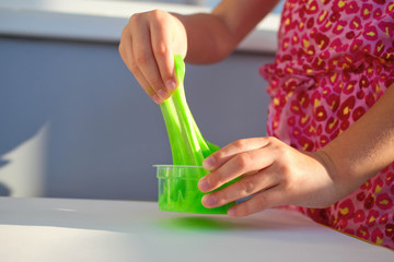 Hand holding homemade toy called Slime, kids having fun and being creative by science experiment. Close up of a little girl is hand playing a green slime